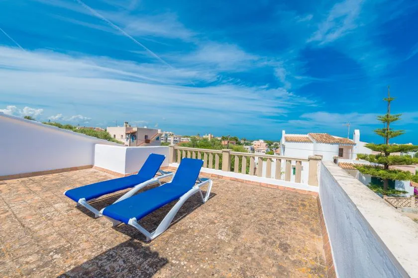 Una terraza soleada en la azotea con tumbonas azules y edificios a lo lejos.