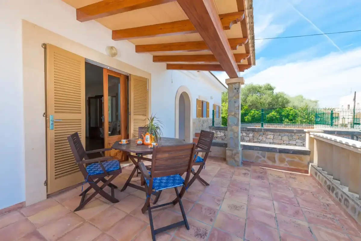 Una terraza exterior embaldosada tiene una mesa de comedor y asientos bajo un voladizo de madera.