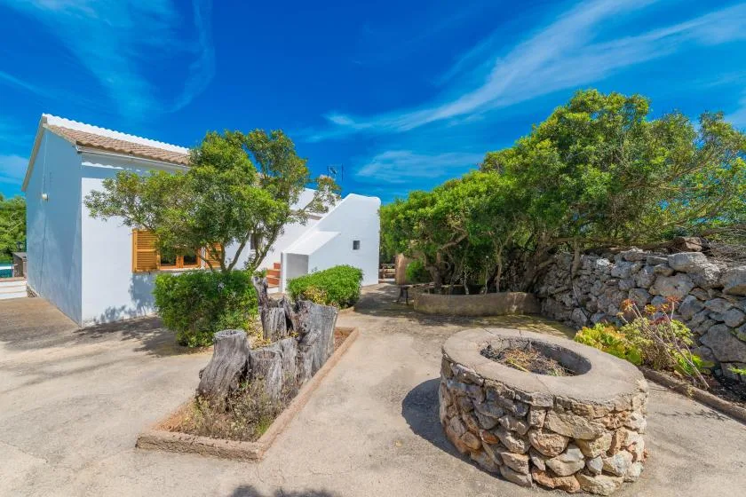 Un edificio blanco junto a un pozo de piedra y un patio arbolado.