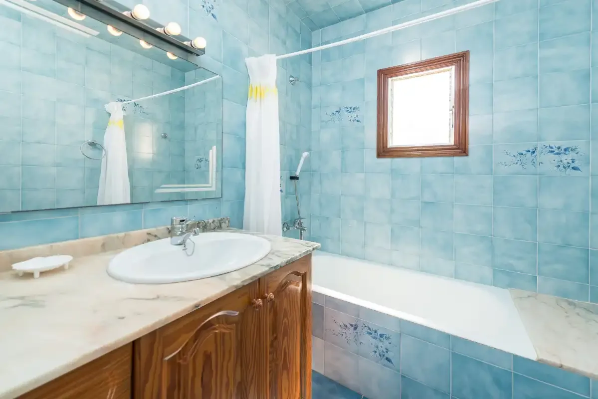 Un baño alicatado con bañera, lavabo y un espejo grande.