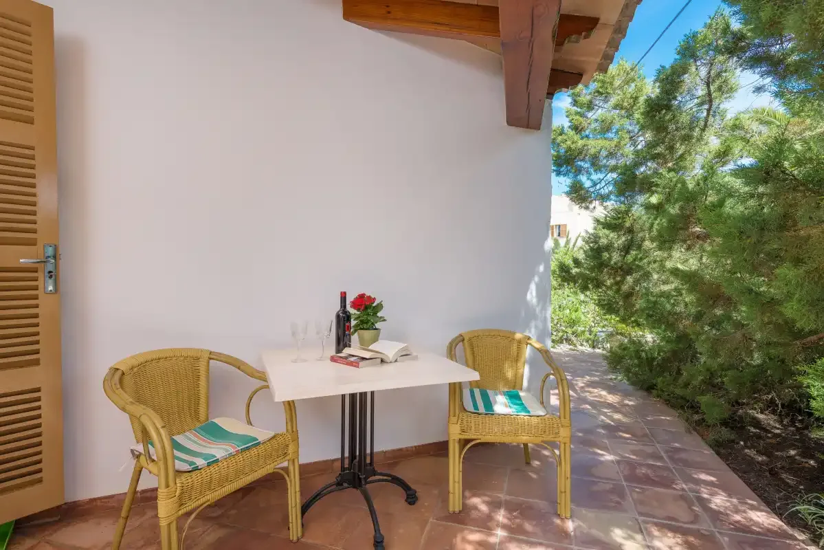 Un pequeño patio exterior con asientos de mimbre y una mesa junto al jardín.