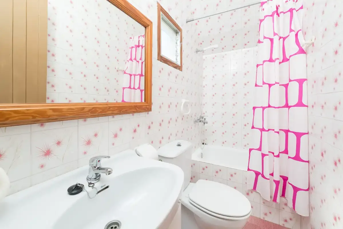 Un baño con lavabo, inodoro y una cortina de ducha rosa brillante.