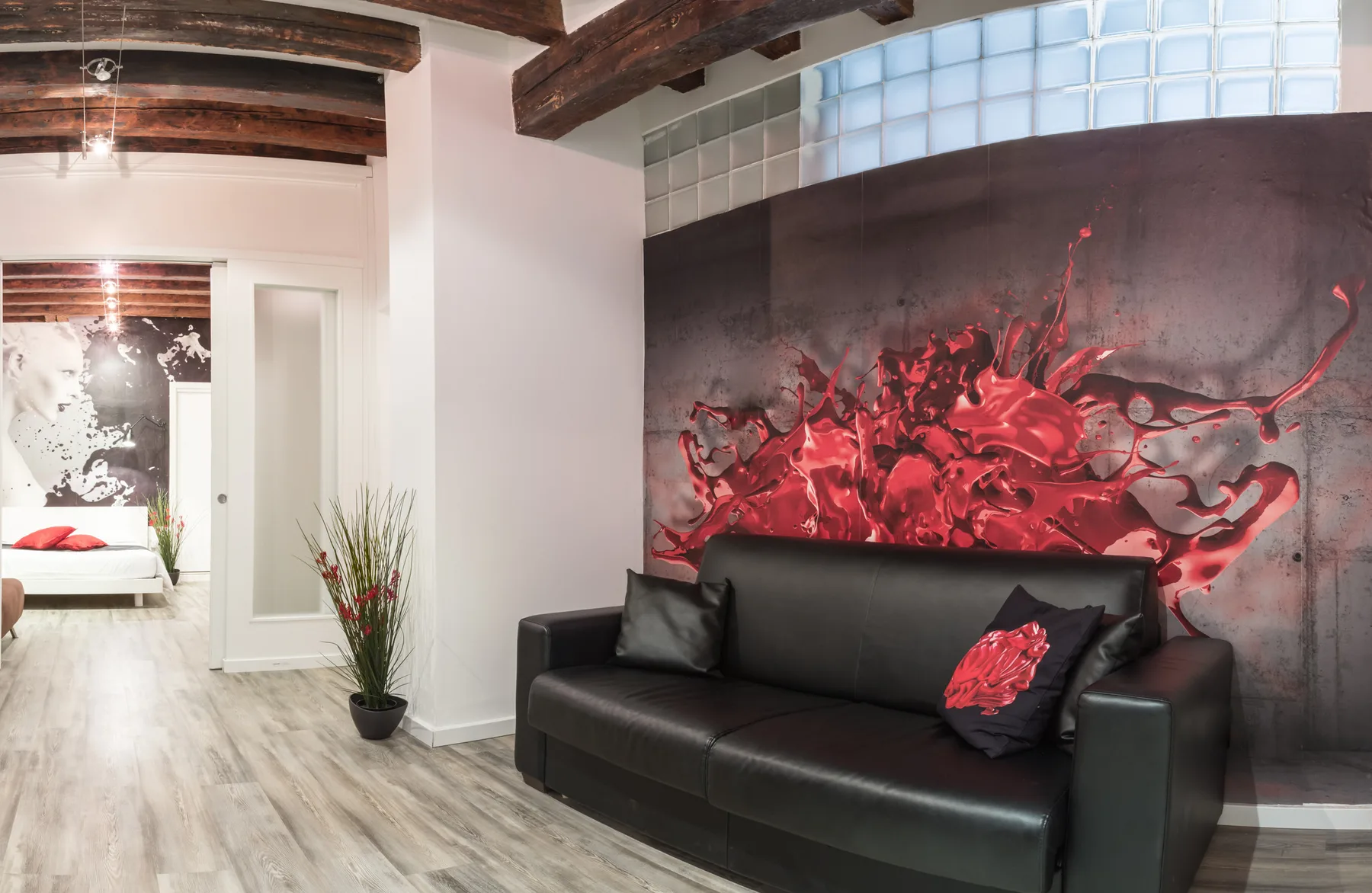 Una sala de estar con un sofá negro frente a un gran mural rojo y negro.