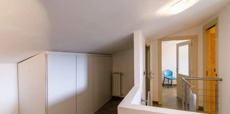 A narrow interior hallway with built-in cupboards and an open doorway to a room with a blue chair.