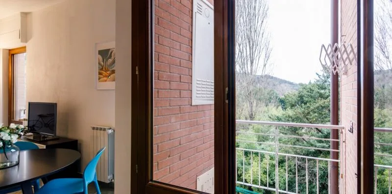 A living area with a television opens onto a balcony overlooking trees.