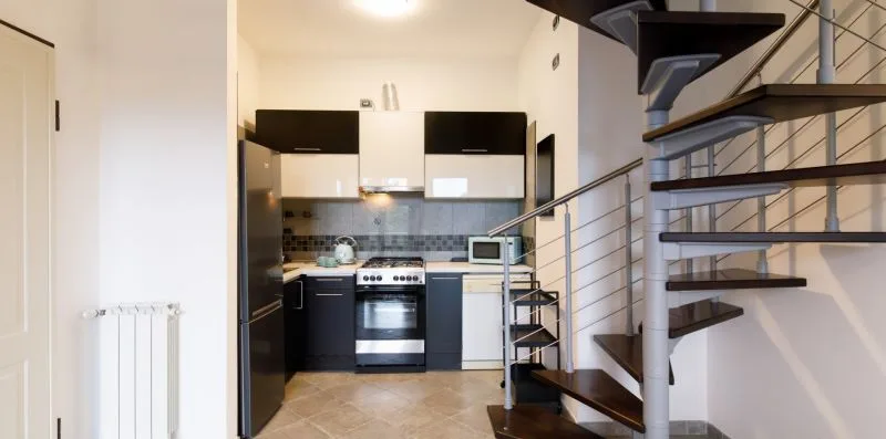 A compact kitchen with dark cabinets and a spiral staircase beside it.