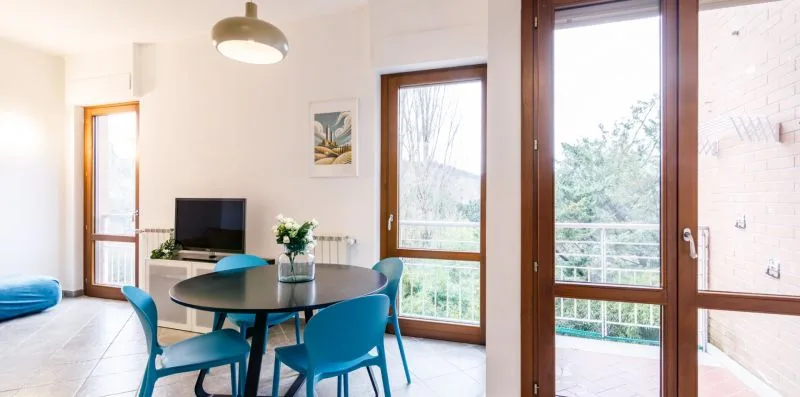 Un luminoso comedor y sala de estar con una mesa, asientos azules y ventanas altas.