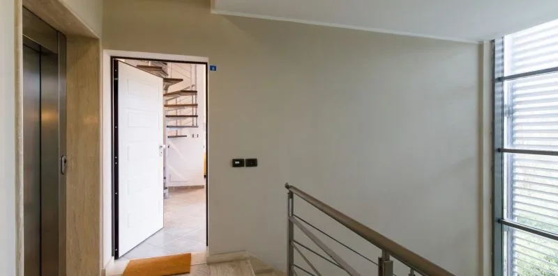 A bright interior hallway with an open doorway and a metal railing.