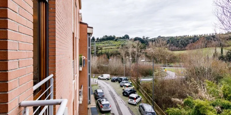 Vista desde un edificio hacia una zona de estacionamiento y colinas arboladas.