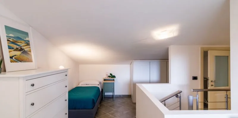 A bedroom with a single bed, dresser, and stair railing.