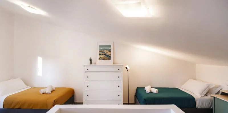 A bedroom with two beds and a white dresser beneath framed artwork.