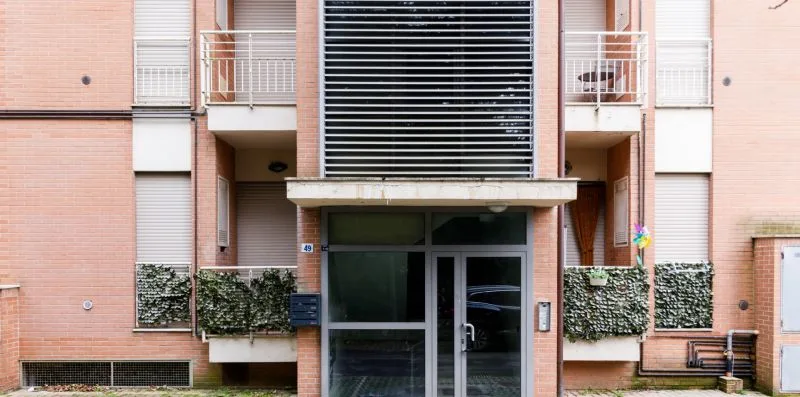 A brick apartment building entrance with glass doors and balconies above.