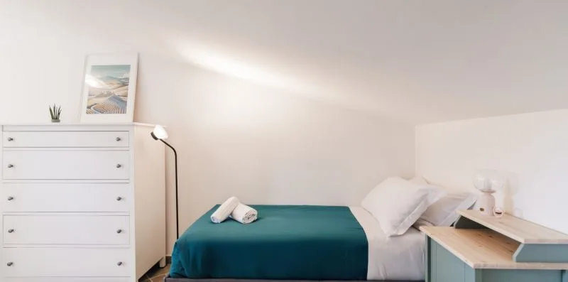 A bedroom with a teal bedspread and a white dresser.