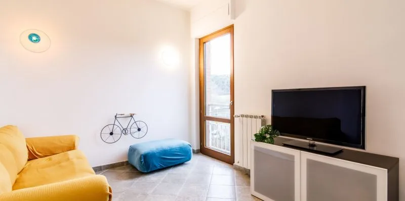 Una sala luminosa con asientos, un televisor y una puerta alta de vidrio.