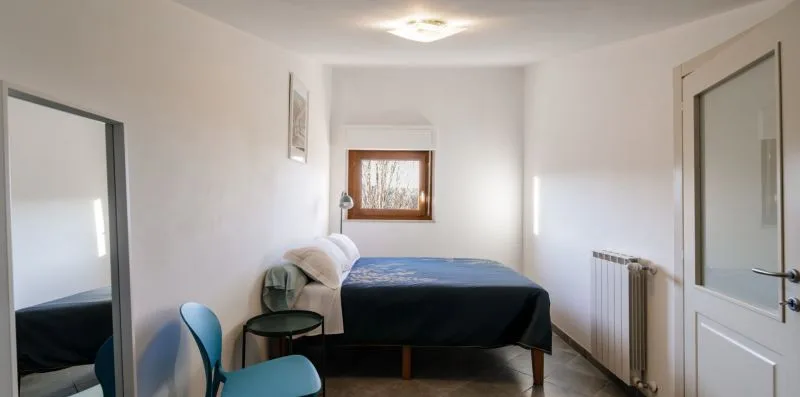 A bedroom with a bed, a small table, and a window.