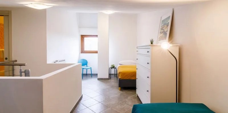 A bright bedroom with a bed, dresser, and small seating area.