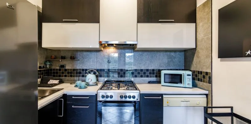 A compact kitchen with dark cabinets, a tiled backsplash, and stainless steel appliances.
