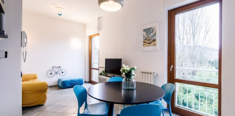 Un comedor luminoso tiene una mesa redonda, asientos azules y una ventana grande.