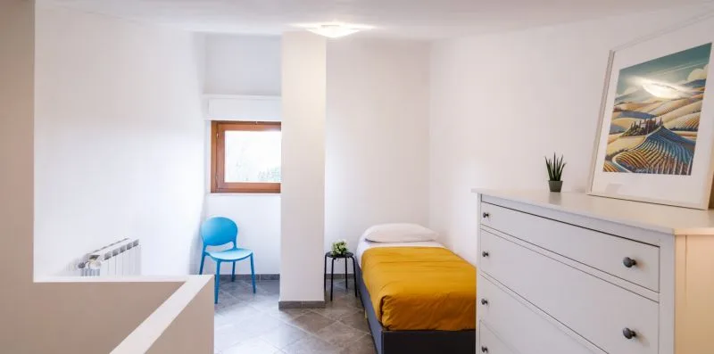 A bright bedroom with a single bed, a blue chair, and a white dresser.