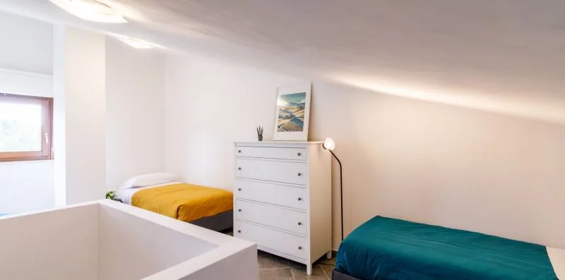 A bright bedroom with two beds and a white chest of drawers.