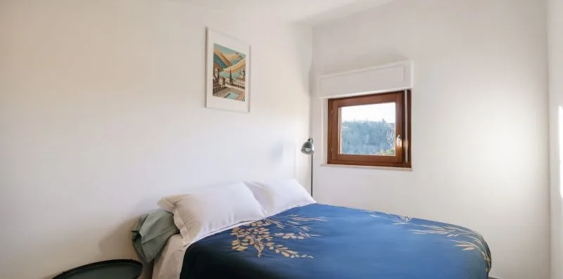 Un dormitorio con una cama cubierta por una colcha azul estampada y una ventana pequeña.