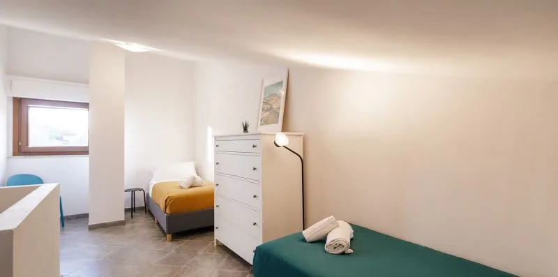 A bright bedroom with beds, a white dresser, and a window.