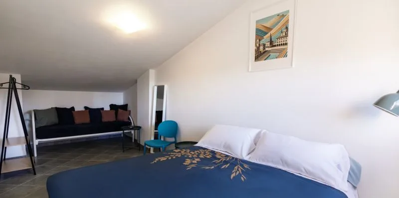 A bedroom with a bed and a seating area along the back wall.