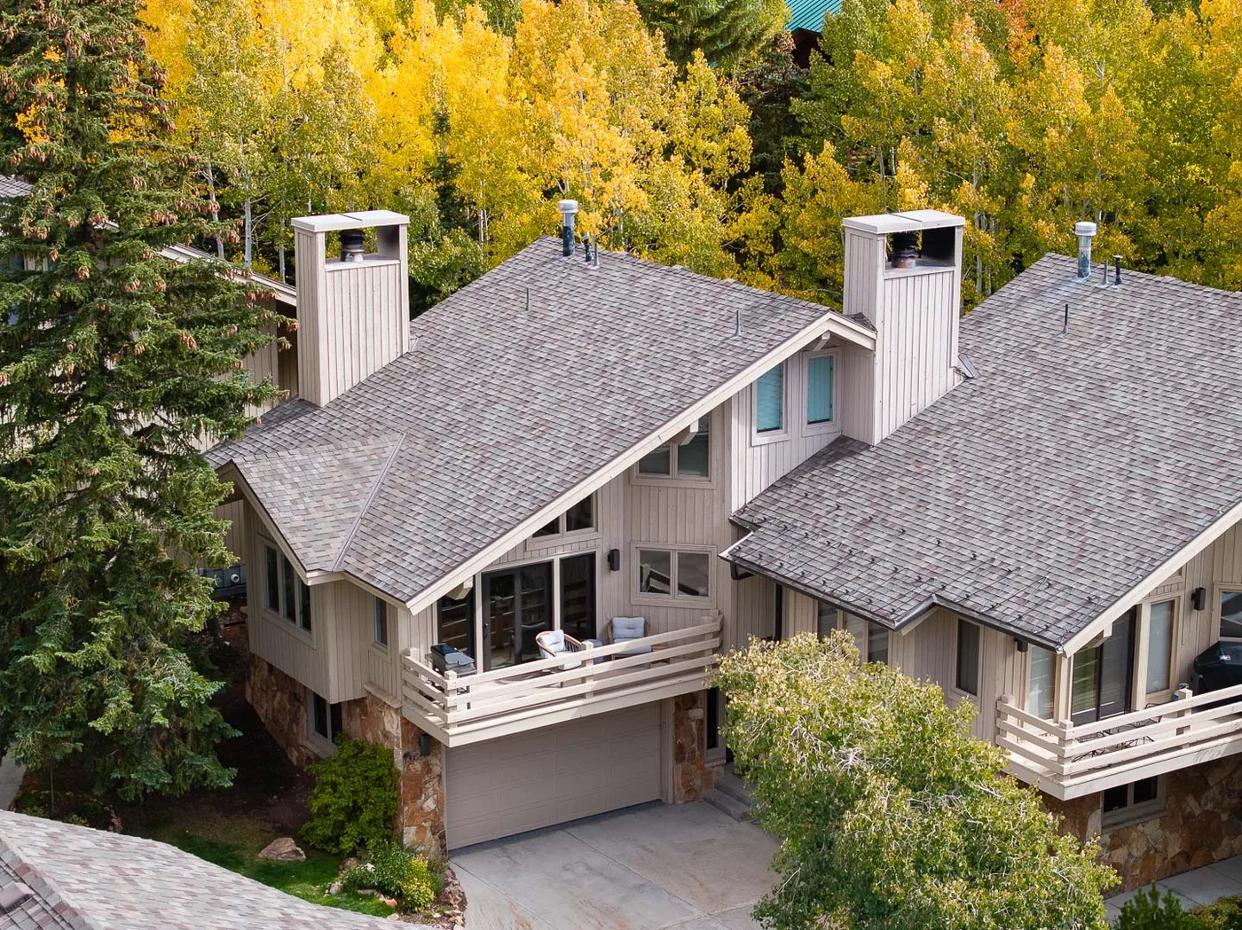 A multi-level house with gray roofs and a balcony sits among autumn trees.