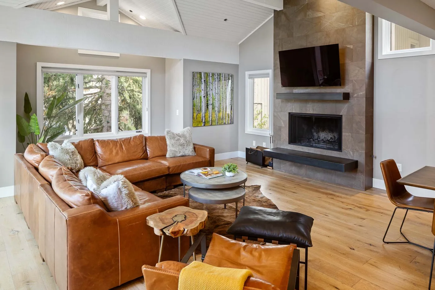 A bright living room with leather seating and a fireplace beneath a wall-mounted television.