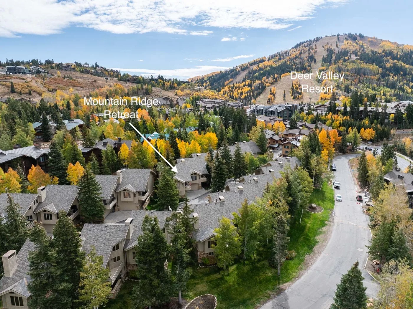 An aerial view of homes among autumn trees, with a mountain resort in the distance.