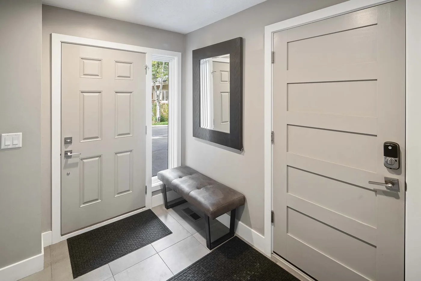 An entryway with two doors, a wall mirror, and a cushioned bench.