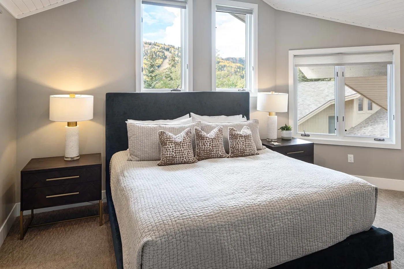 A bedroom with a neatly made bed and windows overlooking a hillside.