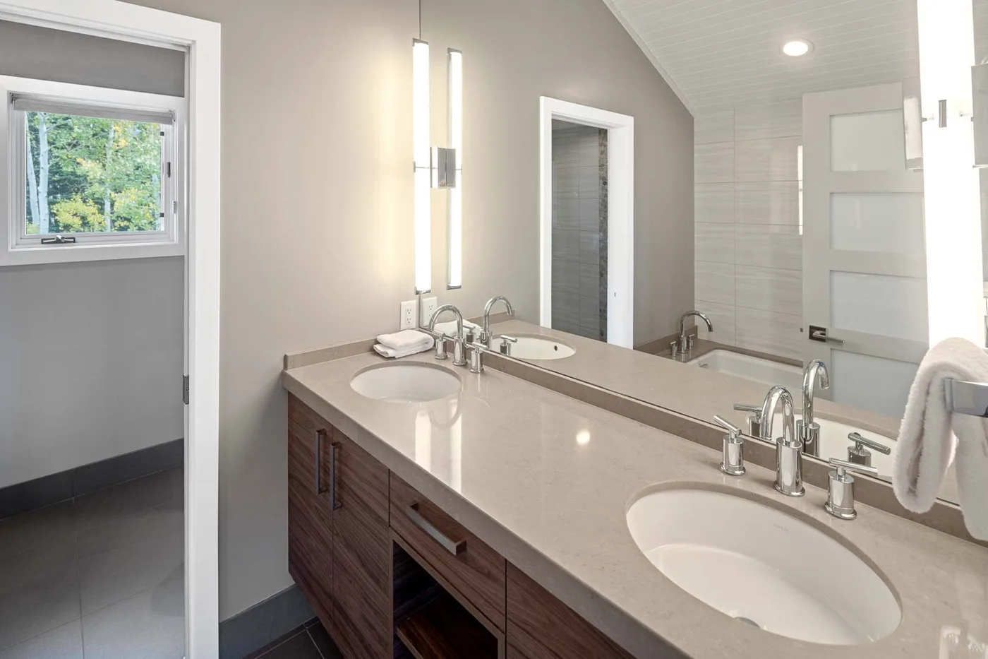 A bright bathroom vanity with two sinks, mirrors, and a window.