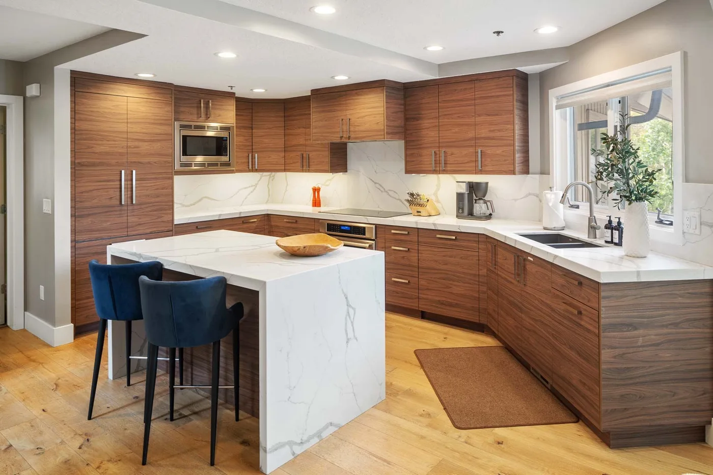A modern kitchen with wood cabinetry, white countertops, and a central island.