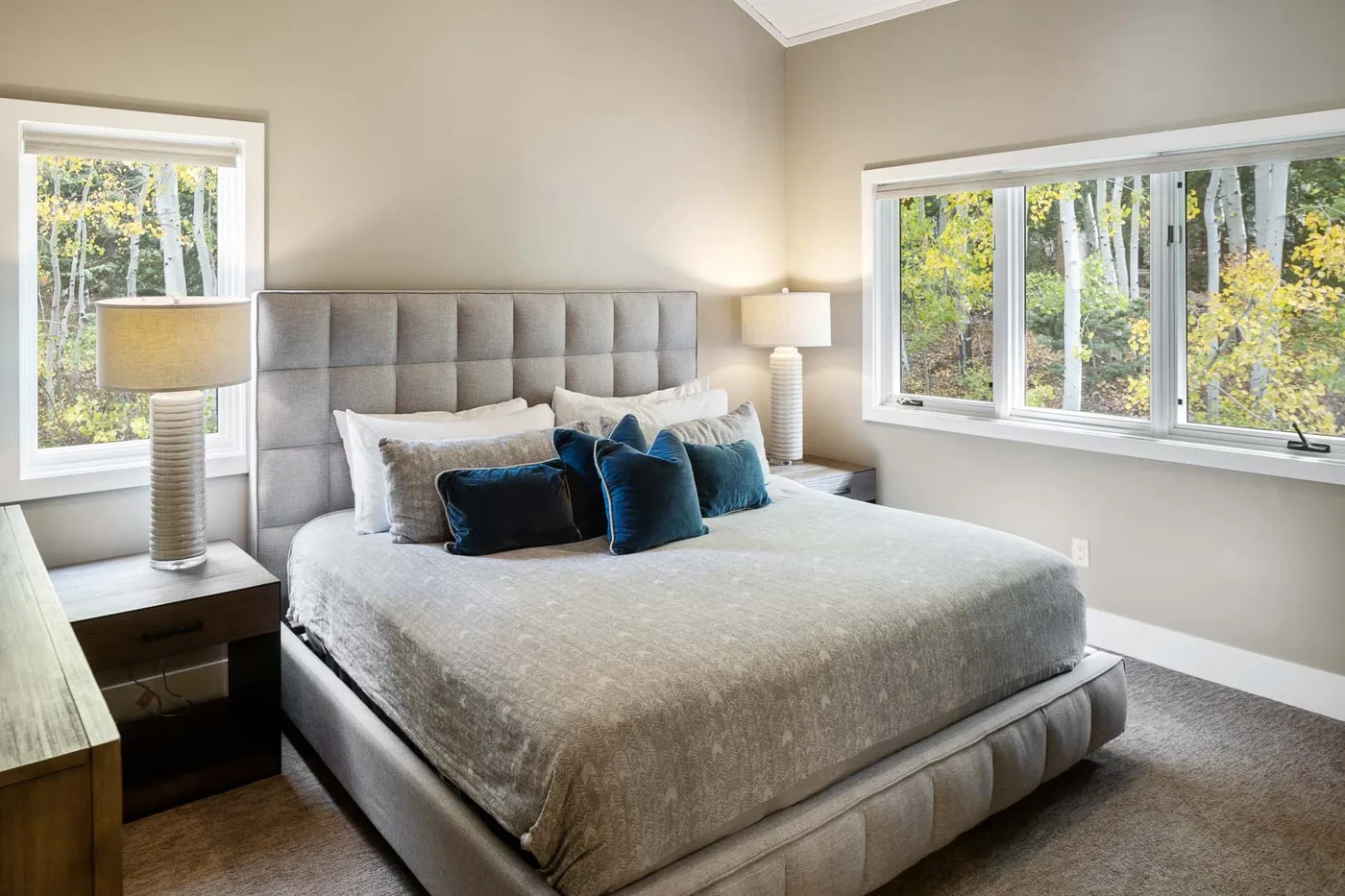 A bedroom with a large bed, bedside tables, and windows overlooking trees.