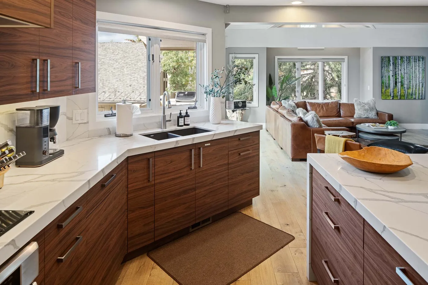 An open kitchen and living area with wood cabinetry and seating by large windows.