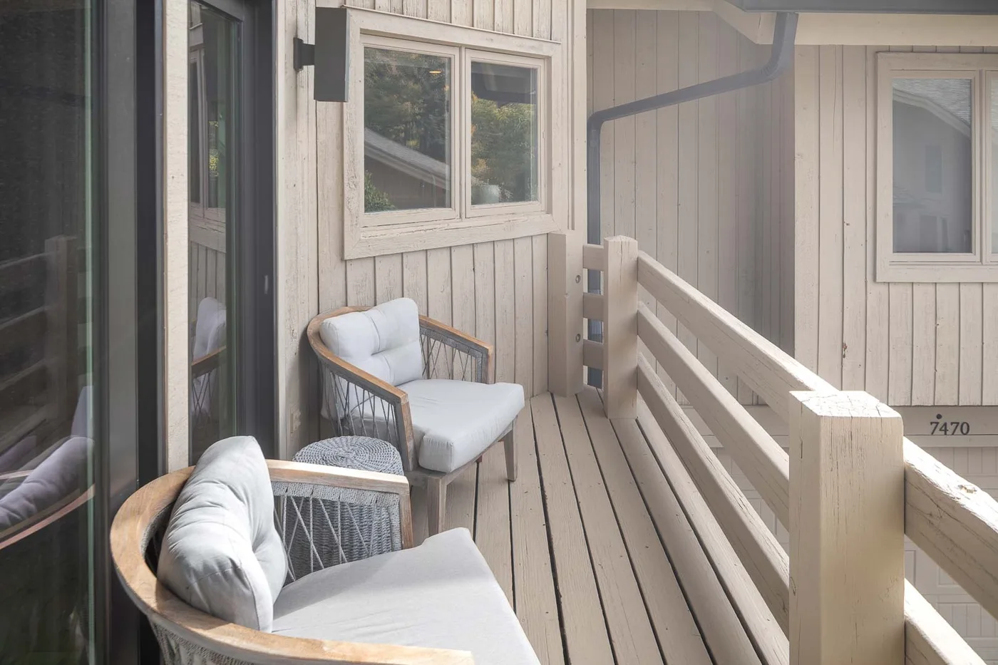 A narrow outdoor balcony with seating, wooden railings, and windows along the wall.