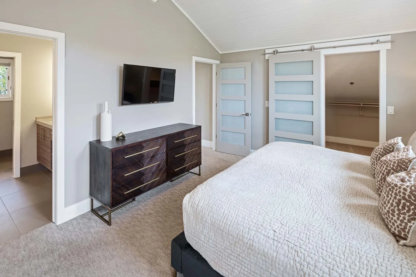 A bedroom with a bed, dresser, and wall-mounted television.