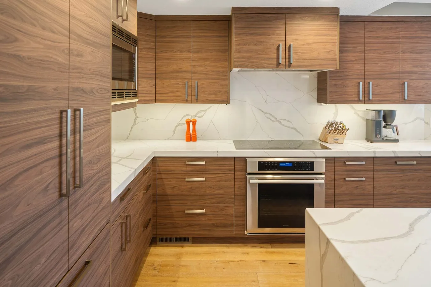 A modern kitchen with wood cabinetry, a built-in oven, and a light stone countertop.