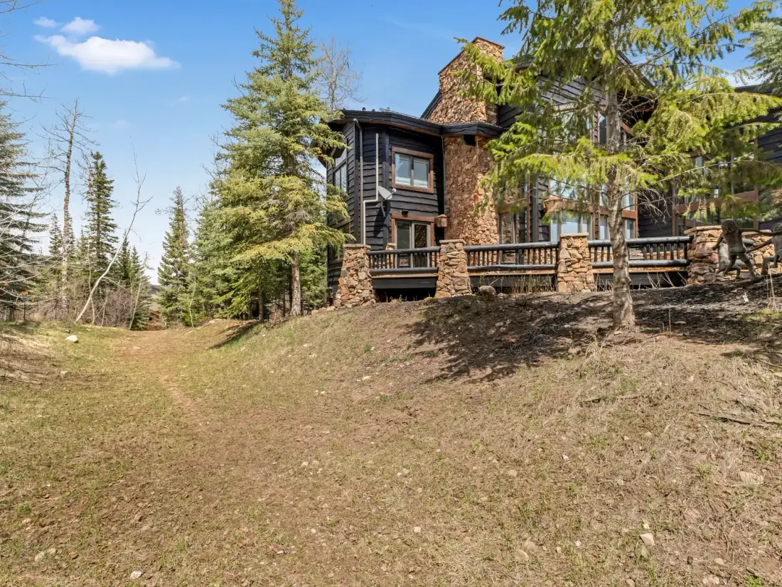 A large house sits among trees above a gently sloping grassy yard.