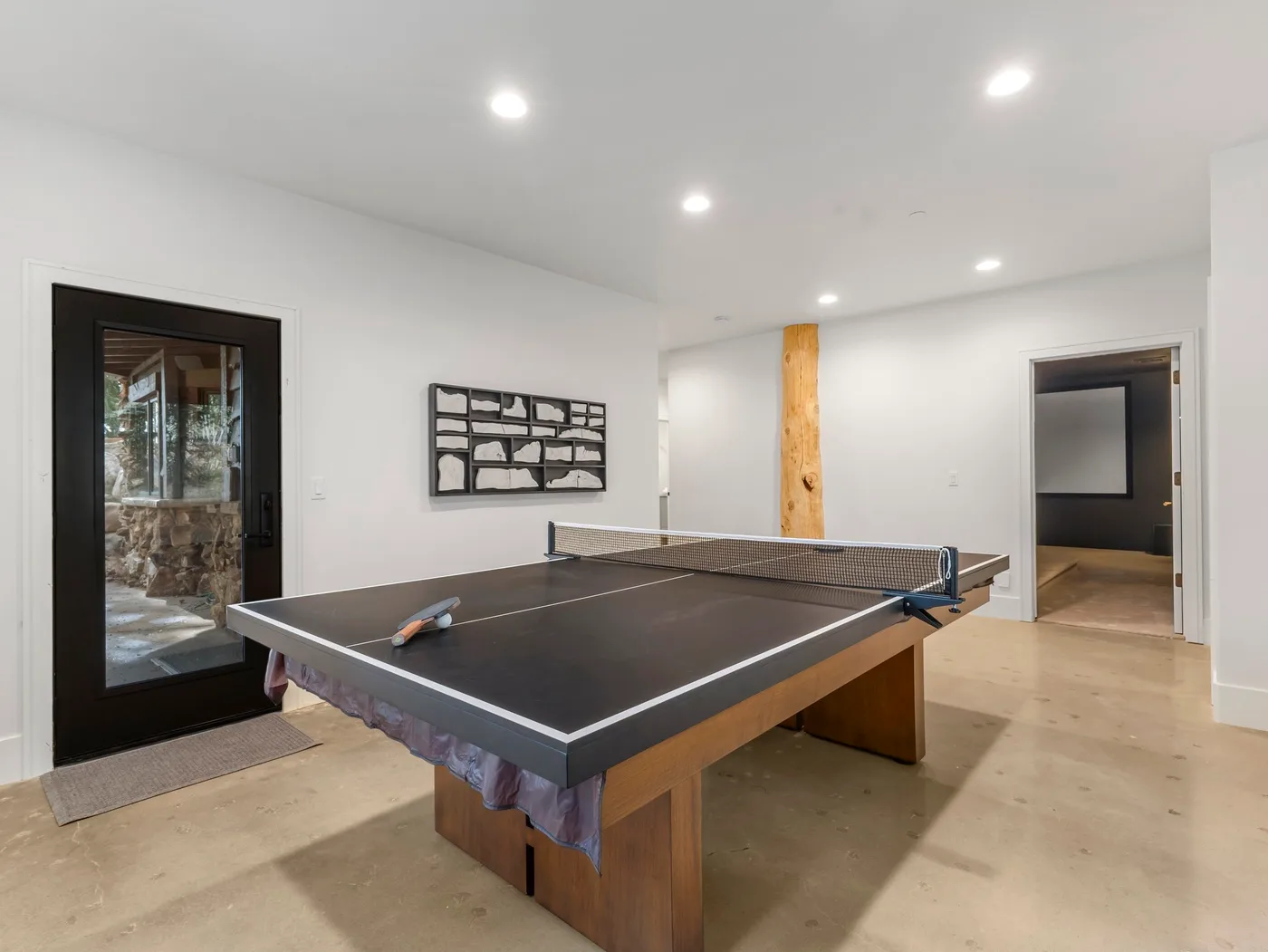 Una mesa de ping-pong ocupa una habitación luminosa con paredes blancas y luces empotradas.