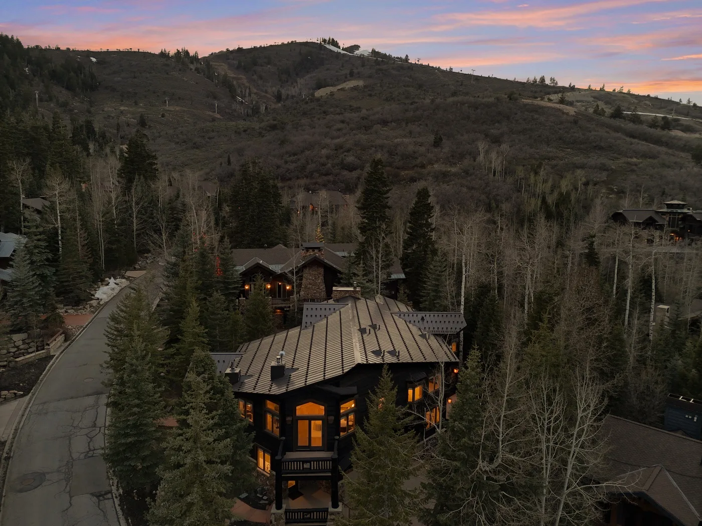 A mountain lodge sits among trees beneath a pink evening sky.