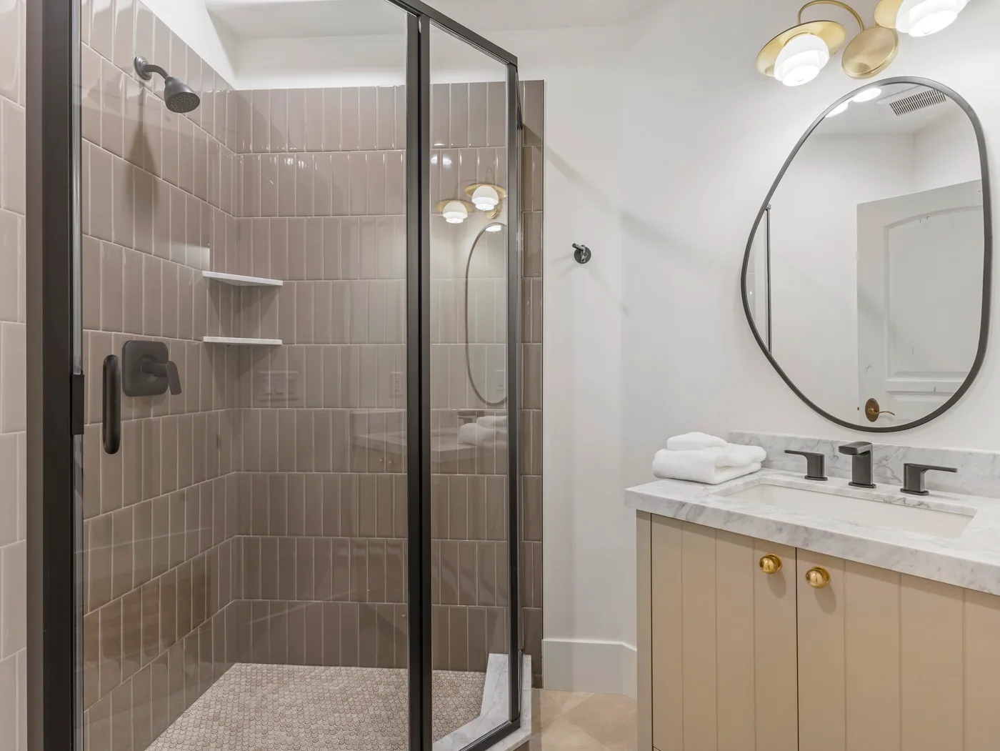 A bathroom with a glass-enclosed shower and a vanity beneath a round mirror.