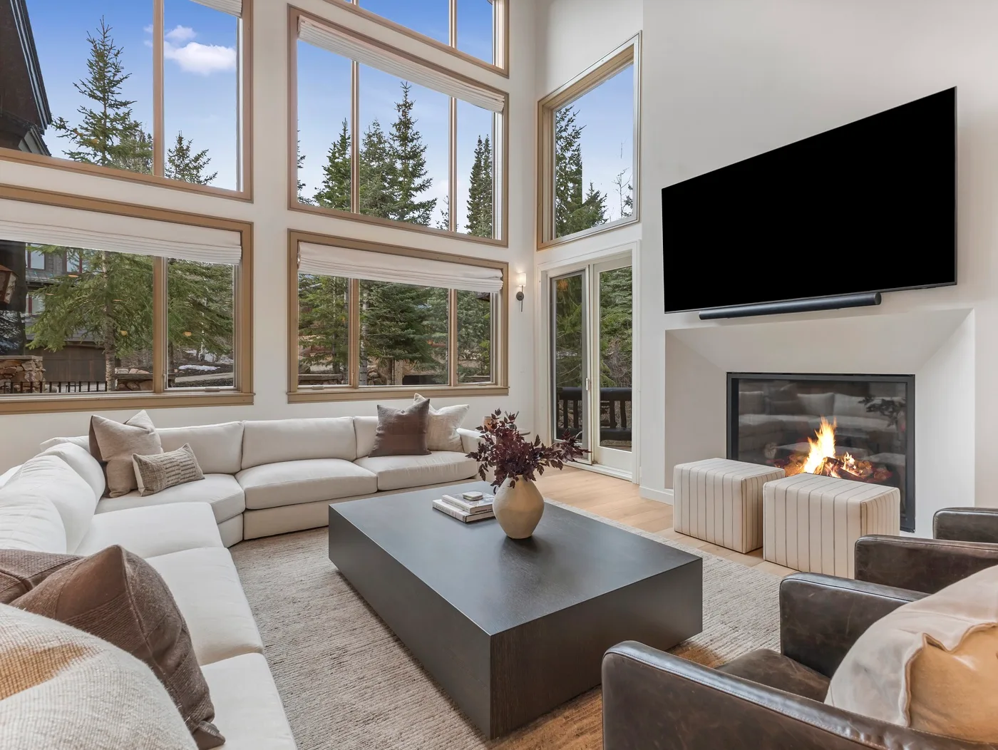A bright living room features large windows, sectional seating, and a fireplace.