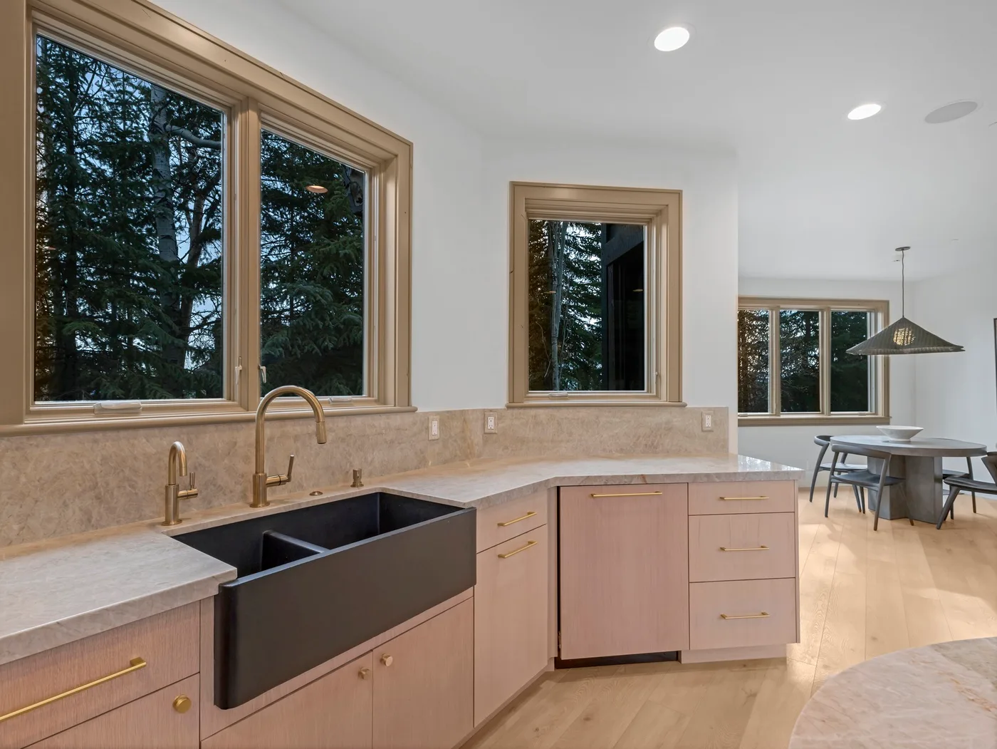 A bright kitchen with a large sink, wood cabinetry, and windows overlooking trees.