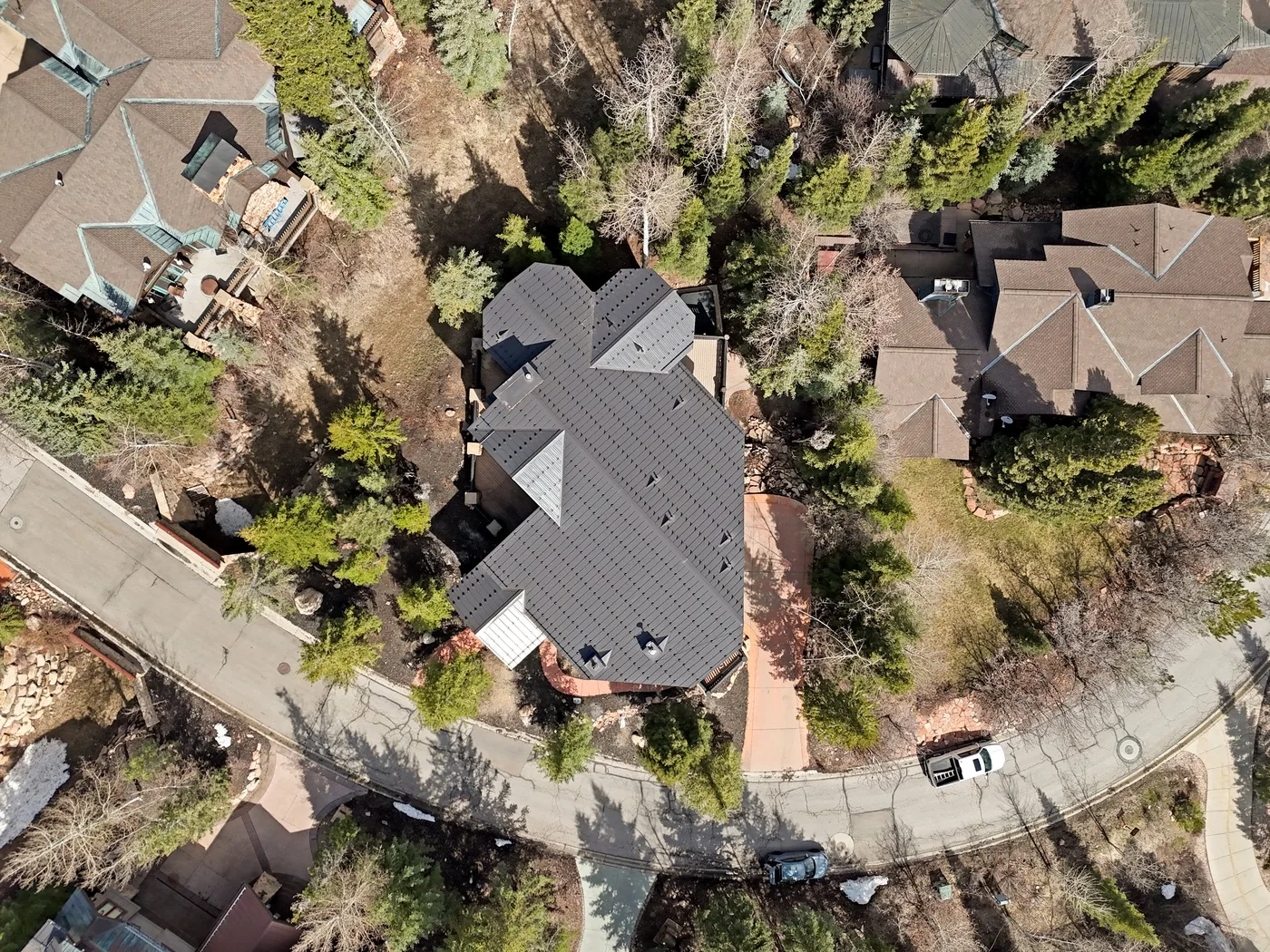 An aerial view of a large house surrounded by trees and neighboring homes.