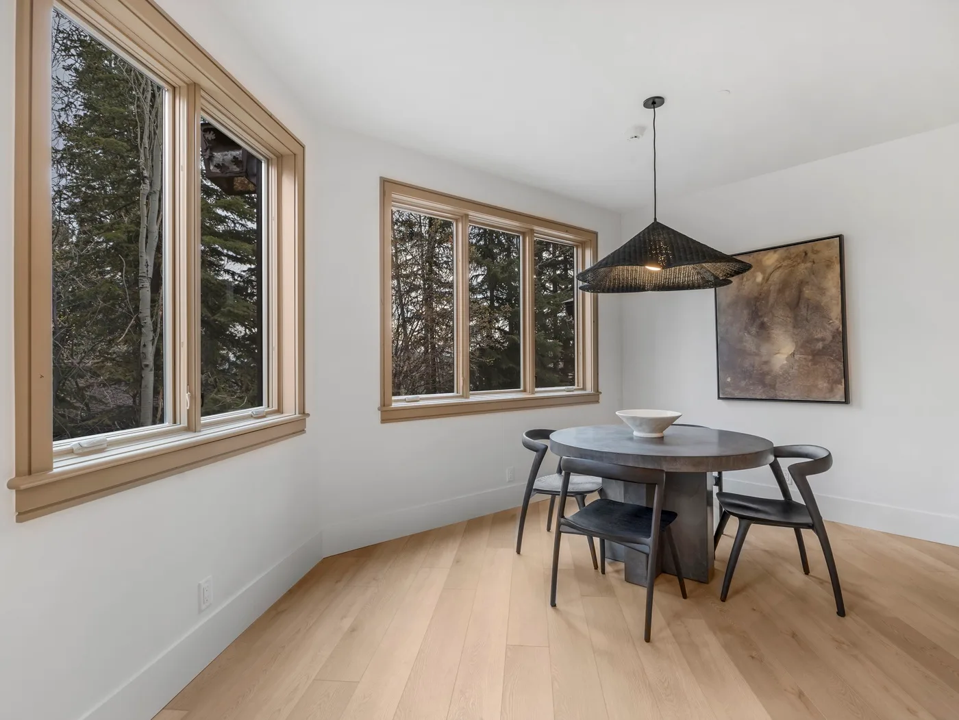A dining area with a round table beneath a hanging light and large windows.