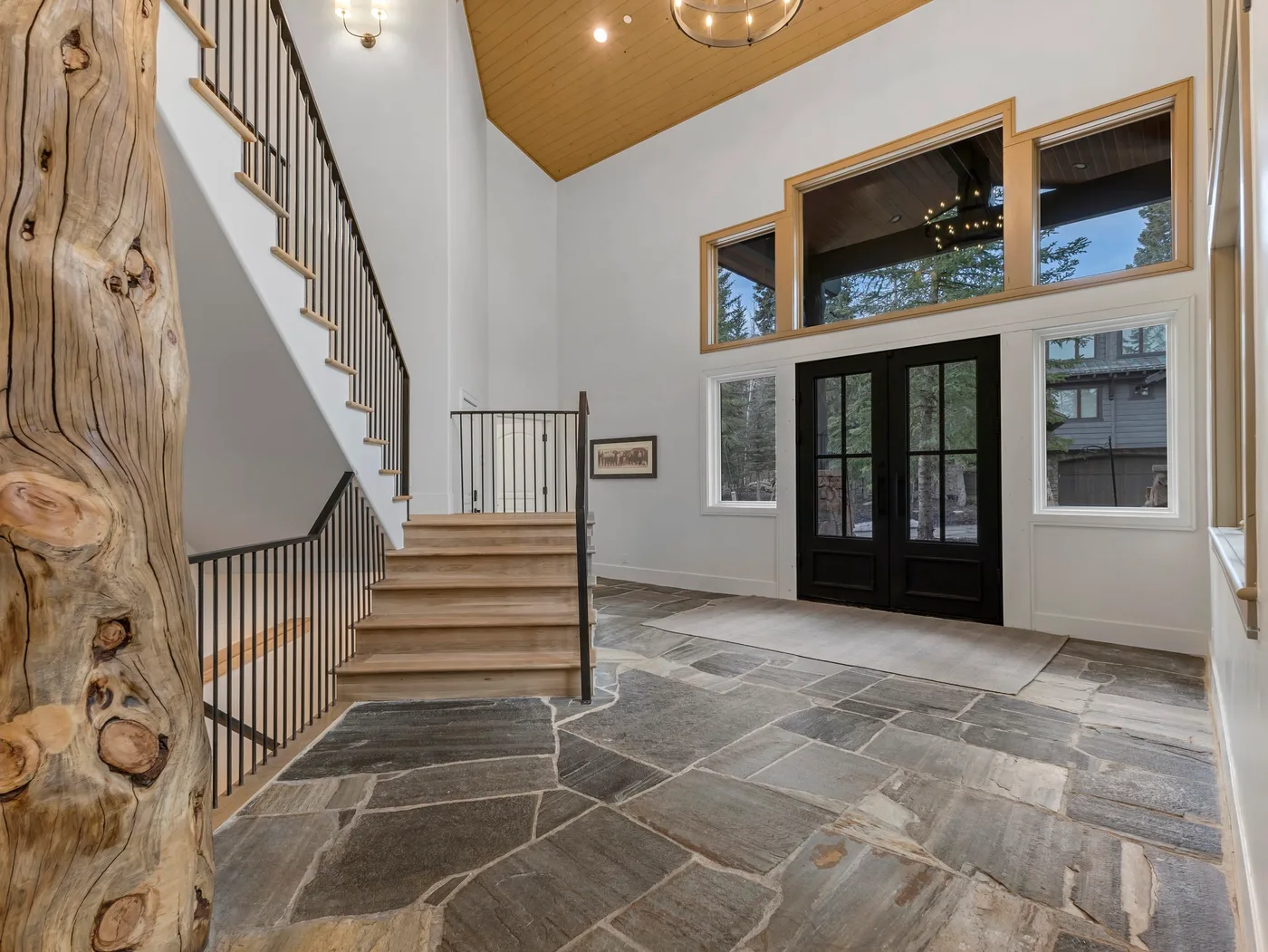 A spacious entry hall with a staircase, stone flooring, and dark double doors.