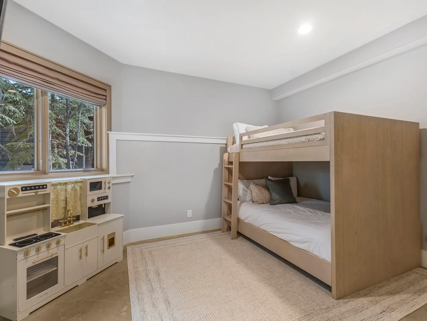 A children’s bedroom with bunk beds and a toy kitchen beside the window.