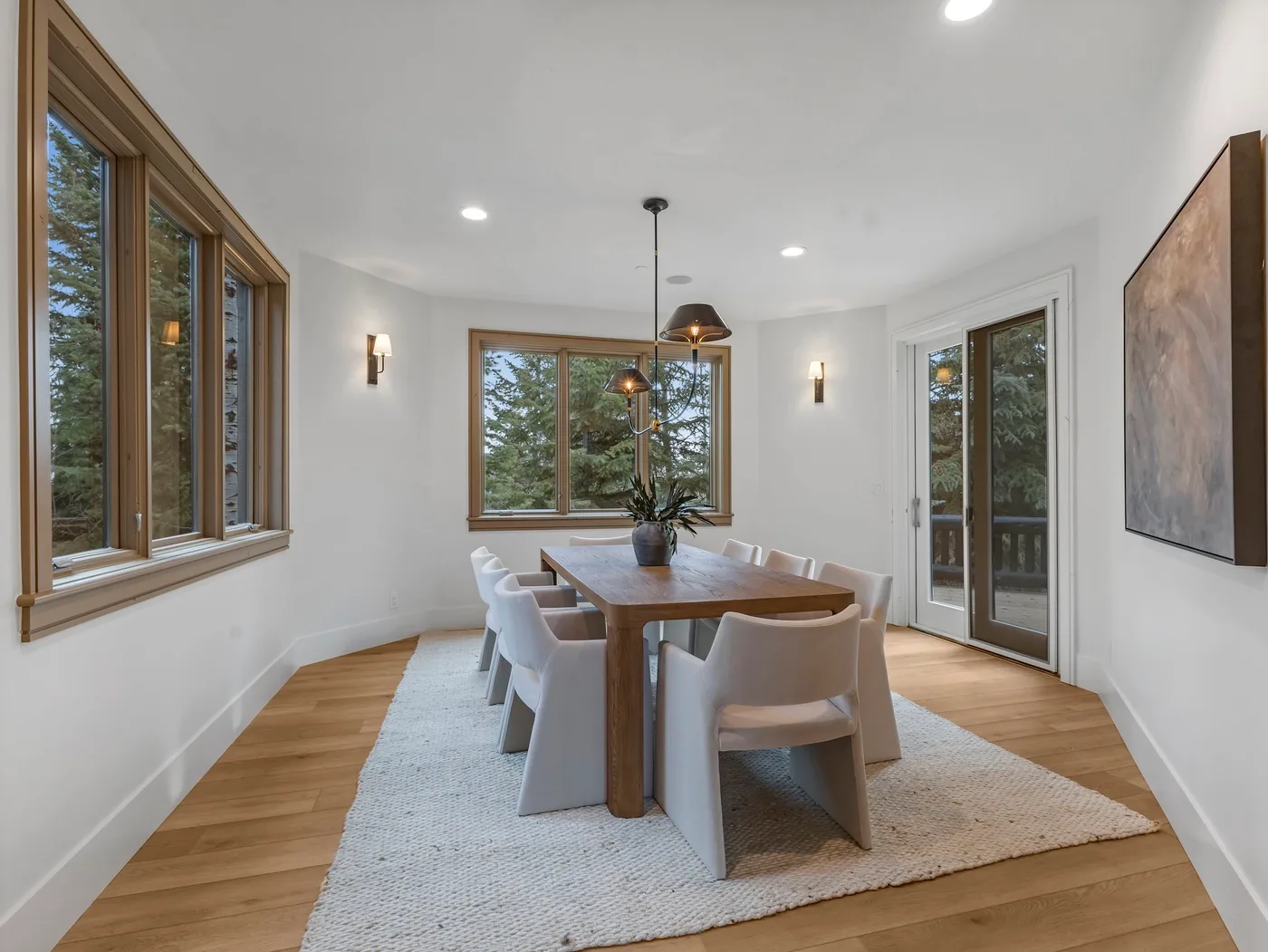 A dining area with a wooden table and large windows overlooking trees.